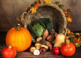 a wicker basket on its side, with an assortment of squash, pumpkins and other vegetables, decorated with fall leaves